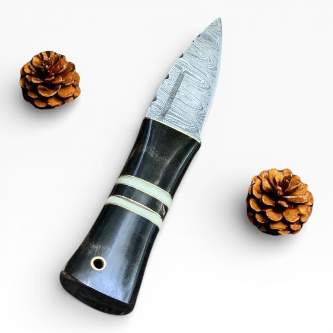Handcrafted knife with a black handle and silver blade, surrounded by pine cones on a white background.